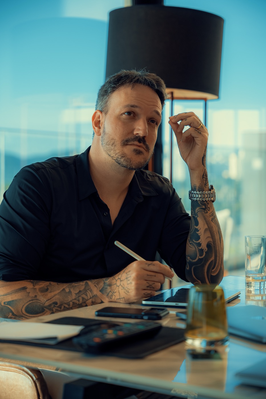 Retrato de Marcelo Pinazza sentado à mesa de trabalho, com caneta na mão e expressão de quem está avaliando um problema