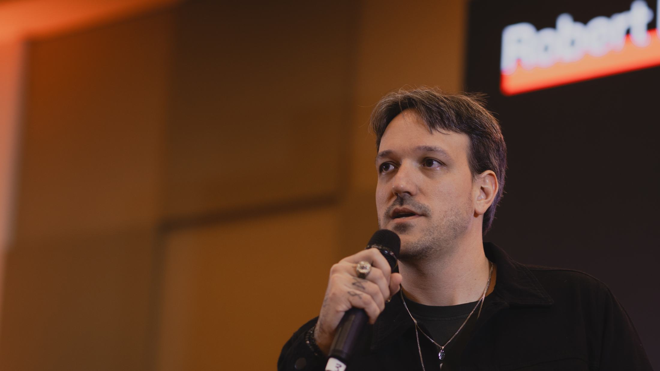 Marcelo Pinazza no palco, com microfone na mão, conduzindo uma apresentação para empresários